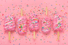 Flat Lay Of Creative Concept Of Popsicle With Sprinkles And Icing Over Pink Background