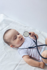 Little cute baby doctor. 6-month old baby boy playing with stethoscope. Kid having fun like a doctor