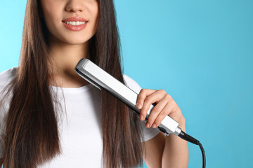 Wall Mural - Happy woman using hair iron on color background, closeup