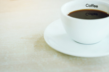 Closeup black coffee in white cup with coffee text insign. Selective focus soft and blurred background