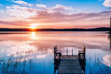 Idyllic View Of The Long Pier With Wooden Bench On The Lake. Sunset Or Sunrise Over The Water.