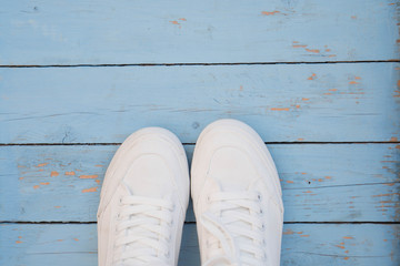 White women's sneakers on a blue boardwalk background. Clean white sneakers in the center of the frame on the blue wooden floor. Trend shoe onthe blue background witn copyspace