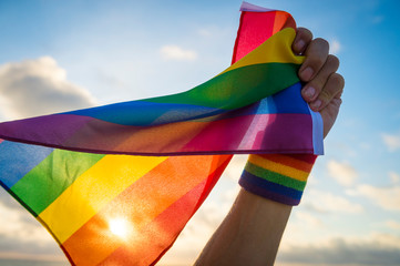 hand with rainbow wristband waving gay pride flag waving backlit in the wind against golden sunset s