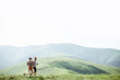© rh2010 - Couple walking with backpacks on the green meadow, traveling in the mountains during the summer time, wide landscape view