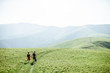 © rh2010 - Couple walking with backpacks on the green meadow, traveling in the mountains during the summer time, wide landscape view