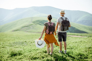 Young couple standing together with backpacks, enjoying beautiful view on the green mountains, rear view