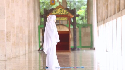 Wall Mural - Side view of young muslim woman praying in mosque while wearing islamic clothes.