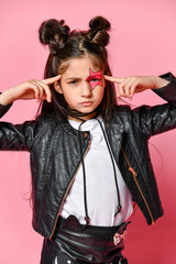 Wall Mural - Portrait of a hipster punk girl - dressed in a leather jacket and skirt, black knee-highs and a white T-shirt, with a funny hairstyle and a makeup painted star on the face, points to the head.