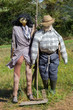 © Nataliia - Two funny scarecrows in the field. Pair of scarecrows with hat and stick. Harvest protection and security concept. Rural landscape. Farm guard. Outdoor security dolls in meadow.