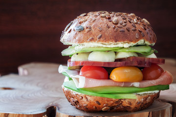 close up pegan  diet snack - homemade hamburger with fresh vegetables and ham between rustic bun bread on the wooden table with dark copy space