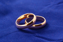 Gold Wedding Rings. Two Engagement Rings Close Up On Blue Velvet Background, Macro Jewelry For Newlyweds.