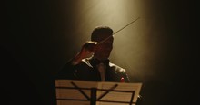 Unrecognizable Male Symphony Orchestra Conductor Wearing Black Tux Is Directing Musicians In Orchestra Pit By Moving His Hands And Baton, Studio Shot On Black Background 4k Footage