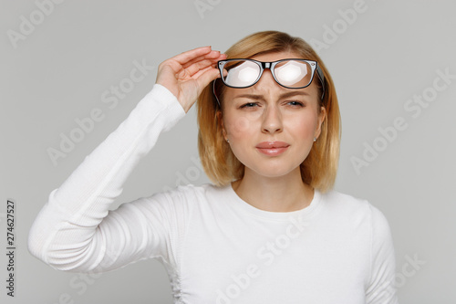 Fotografía Woman has problems with poor eyesight, squinting while trying to see something, taking off glasses, isolated on grey background