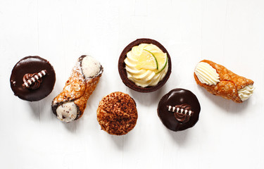 Different pastries on blue background: cannoli with ricotta, tartlets filled with citrus cream, fudge cake, tiramisu cake. Top view