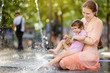 Portrait of beautiful disabled girl in the arms of his mother having fun in fountain of public park at sunny summer day. Child cerebral palsy.