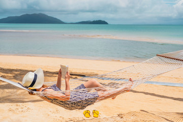 Woman reading a book on hammock beach in free time summer holiday