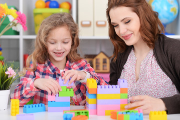 Wall Mural - Cute little girl and her mother playing colorful plastic blocks