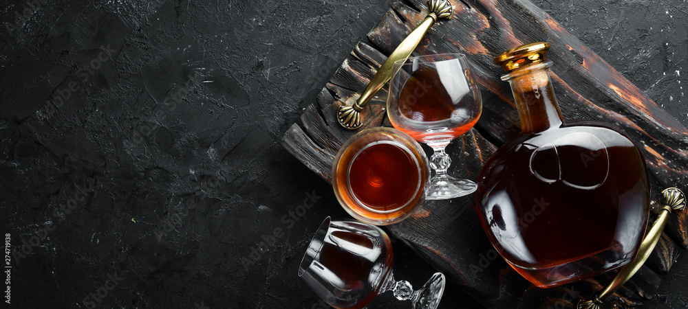 A bottle of cognac and glasses on a black background. Brandy. Top view. Free space for your text. - obrazy, fototapety, plakaty 