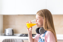 Girl With Headphones Drinking Orange Juice In The Kitchen