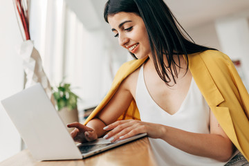 Wall Mural - Cheerful attractive young businesswoman work alone in white room. Remote work. Sit at coworking space. Smiling. Positive nice model typing on keyboard.