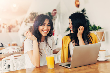 Wall Mural - Cheerful positive female partners in coworking space. Working together. Posing on camera and smile. Bright light in white room. Orange juice on table.