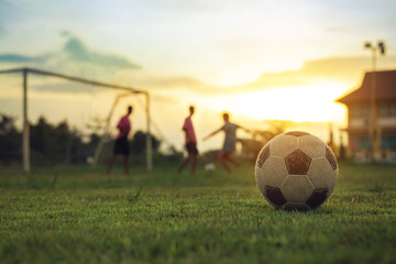 Wall Mural - Silhouette action sport outdoors of a group of kids having fun playing soccer football for exercise in community rural area under the twilight sunset sky.