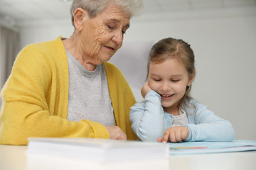 Canvas Print - Cute girl and her grandmother reading book at home