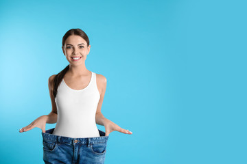 Poster - Attractive young woman with slim body wearing her old big jeans on color background. Space for text