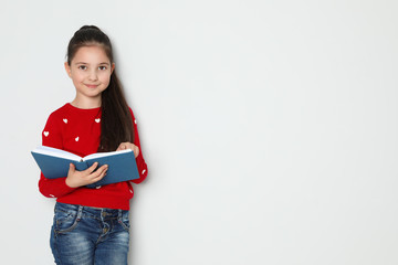 Wall Mural - Cute little girl reading book on white background, space for text