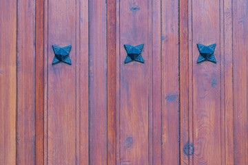 Wooden texture background. Closeup of a detail from a wooden red brown entrance door with three metal stars on the wooden planks. Macro.