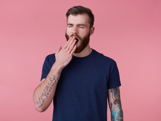 Wall Mural - Photo of young handsome tired red bearded manman in blank t-shirt, wonts to sleep and yawns, stands over pink background with wide open mouth and eyes.