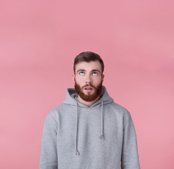 Wall Mural - Portrait of young tired handsome guy looking up at the copy space, thinking about solving a problem, presents possible options, stands over pink background.