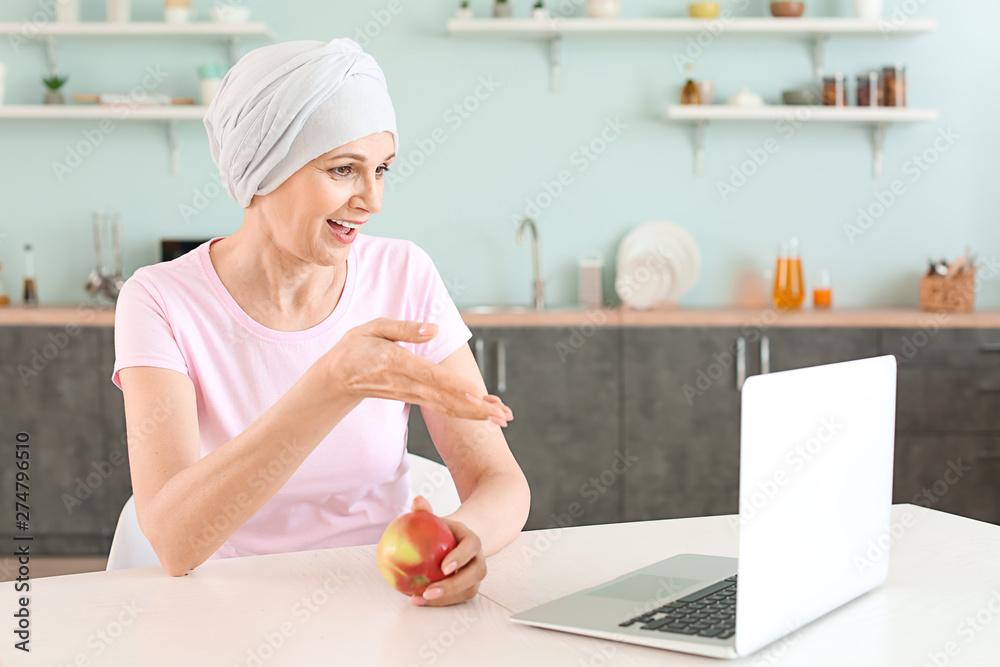 Mature woman after chemotherapy using laptop in kitchen at home