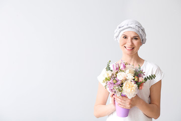 Poster - Woman after chemotherapy with bouquet of flowers on light background