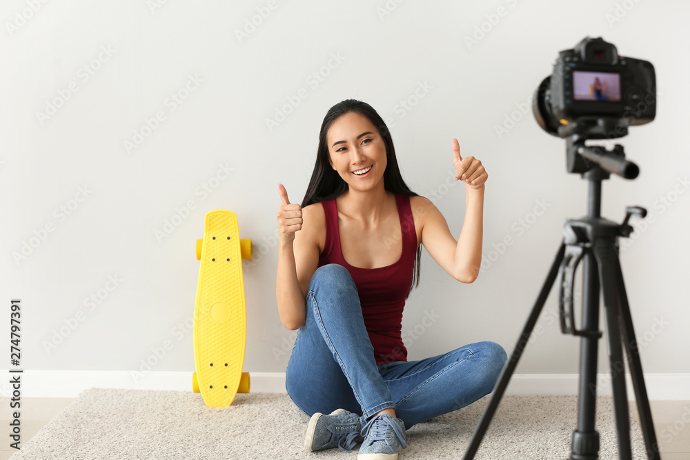 Female Asian blogger recording video near light wall
