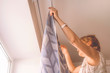 © Mihail - adult housewife hanging the curtains standing on the ladder at home