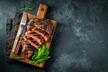 Sliced Steak Ribeye, Grilled With Pepper, Garlic, Salt And Thyme Served On A Wooden Cutting Board On A Dark Stone Background. Top View With Copy Space. Flat Lay