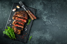 Sliced Steak Ribeye, Grilled With Pepper, Garlic, Salt And Thyme Served On A Slate Cutting Board On A Dark Stone Background. Top View With Copy Space. Flat Lay
