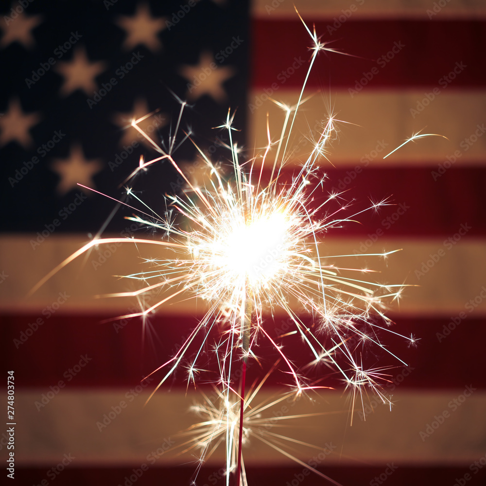 Lit sparkler in front the American Flag for 4th of July celebration ...