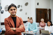 © Seventyfour - Waist up portrait of mixed-race young man smiling at camera confidently with group of students in background, copy space