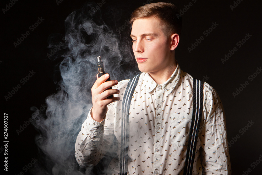 Vaping. Elegant guy with a vape. A man blows smoke from vaping. A man  smokes an electronic cigarette. Smoke break. Stock Photo