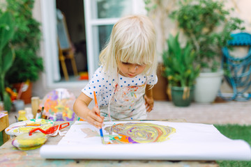 Little cute girl painting in the garden and mixing different colors