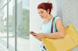 © DragonImages - Beautiful young woman with big bag standing at wall and texting friends