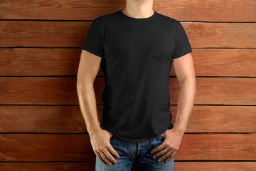 Sport slim man iin a black T-shirt and blue jeans on a brown wooden studio background.