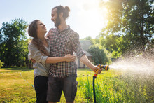 Young Beautiful Couple Watering The Plants In A Country House, Summer, Work In The Garden, Love And Summer Concept