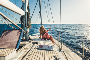 People enjoy travel adventure with alternative transportation way - beautiful curly blonde woman sit down on a sail boat with ocean and sky around - enjoying holiday vacation and luxury lifestyle