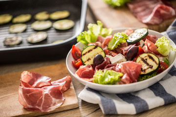 Fresh lettuce salad with grilled zucchini coppa di parma ham feta cheese olives tomatoes and olive oil