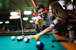 © NDABCREATIVITY - Young couple playing snooker together in bar