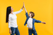 © ViDi Studio - Cheerful woman in casual clothes have fun with child boy. Mother, little kid son jumping, holding hands isolated on yellow orange background. Mother's Day, love family, parenthood childhood concept.