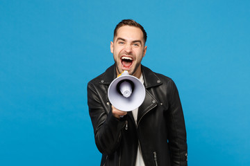 Handsome young unshaven man in black jacket white t-shirt scream in megaphone, announces discounts sale isolated on blue wall background studio portrait. People lifestyle concept. Mock up copy space.